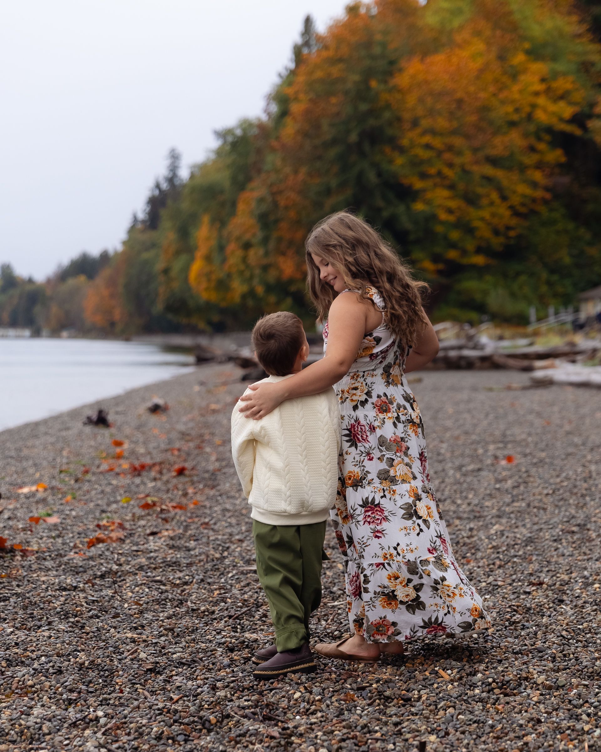 Sister and brother hug during a fall family session with orange fall foliage at Owen Beach in Tacoma.