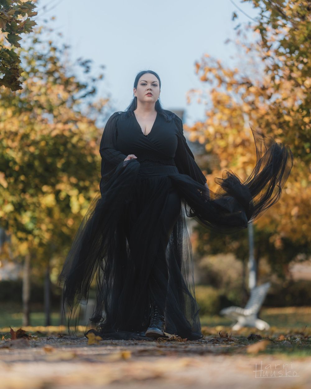 Dramatic portrait in flowing black dress with autumn leaves and trees in background.