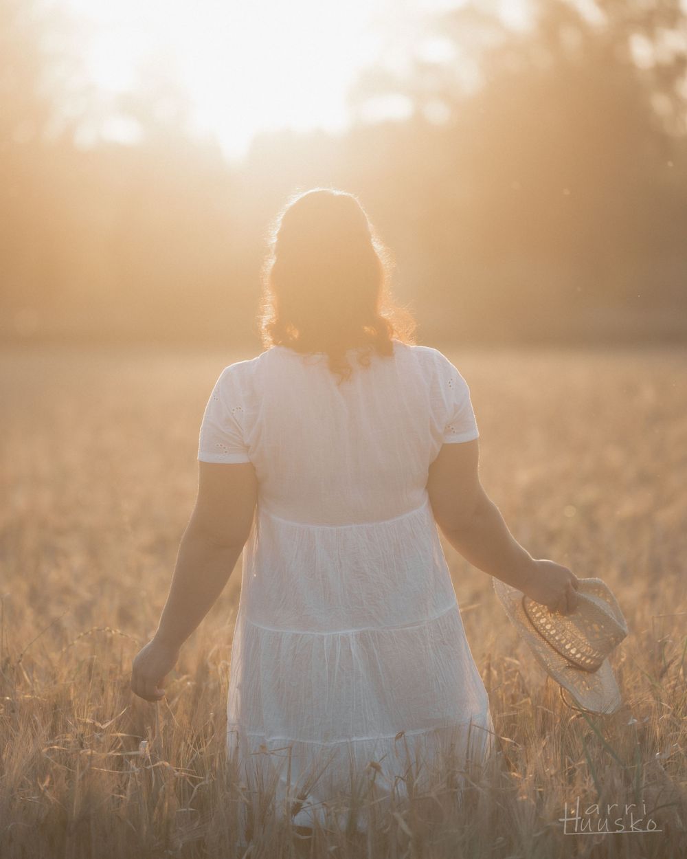 Person in white dress walking through golden wheat field at sunset.