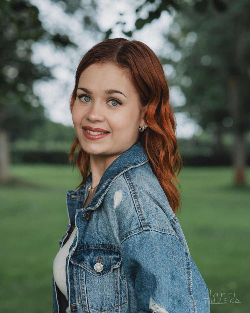 Portrait of woman in denim jacket smiling outdoors.
