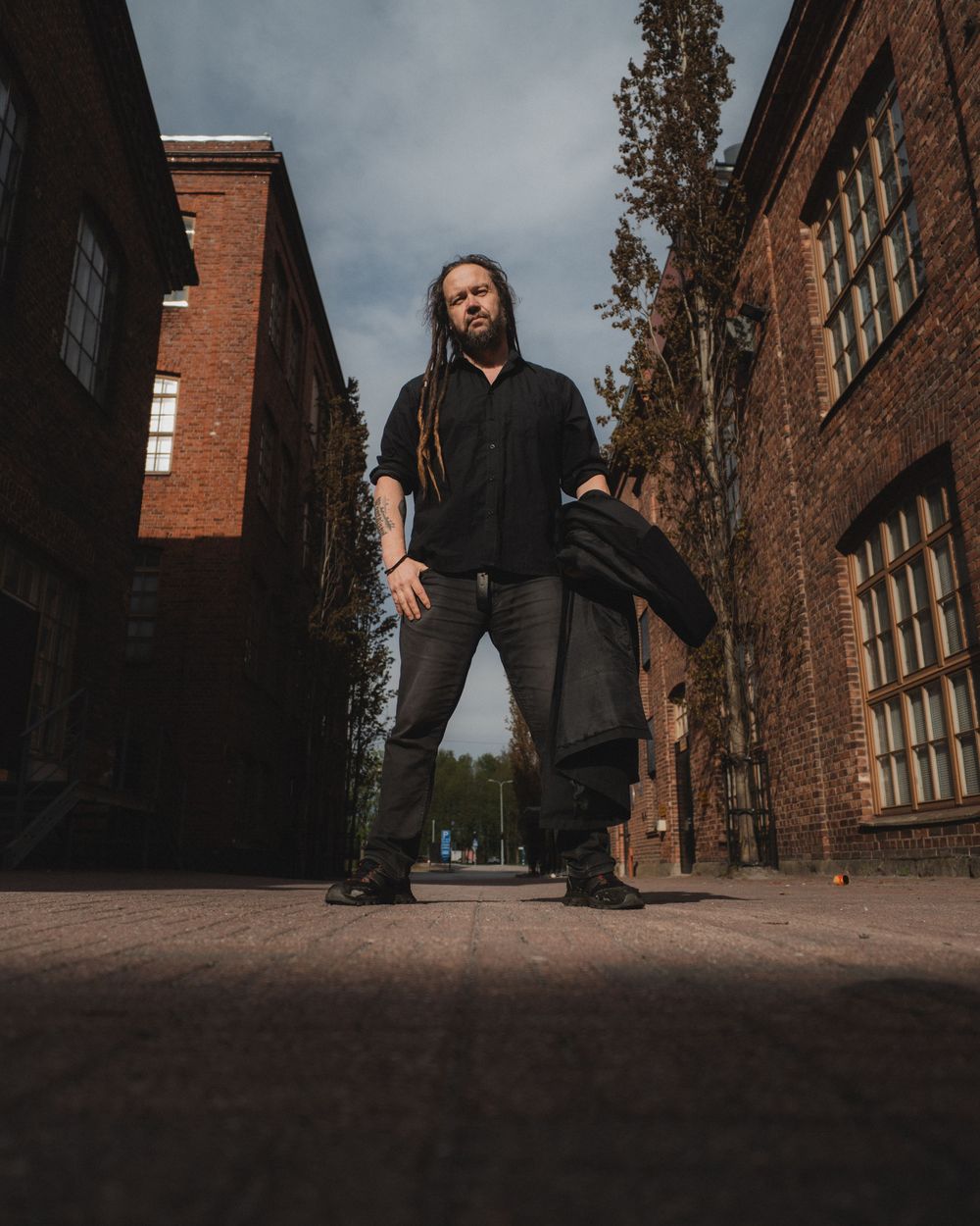 A person in black clothing is photographed from a low angle against brick buildings and cloudy sky.