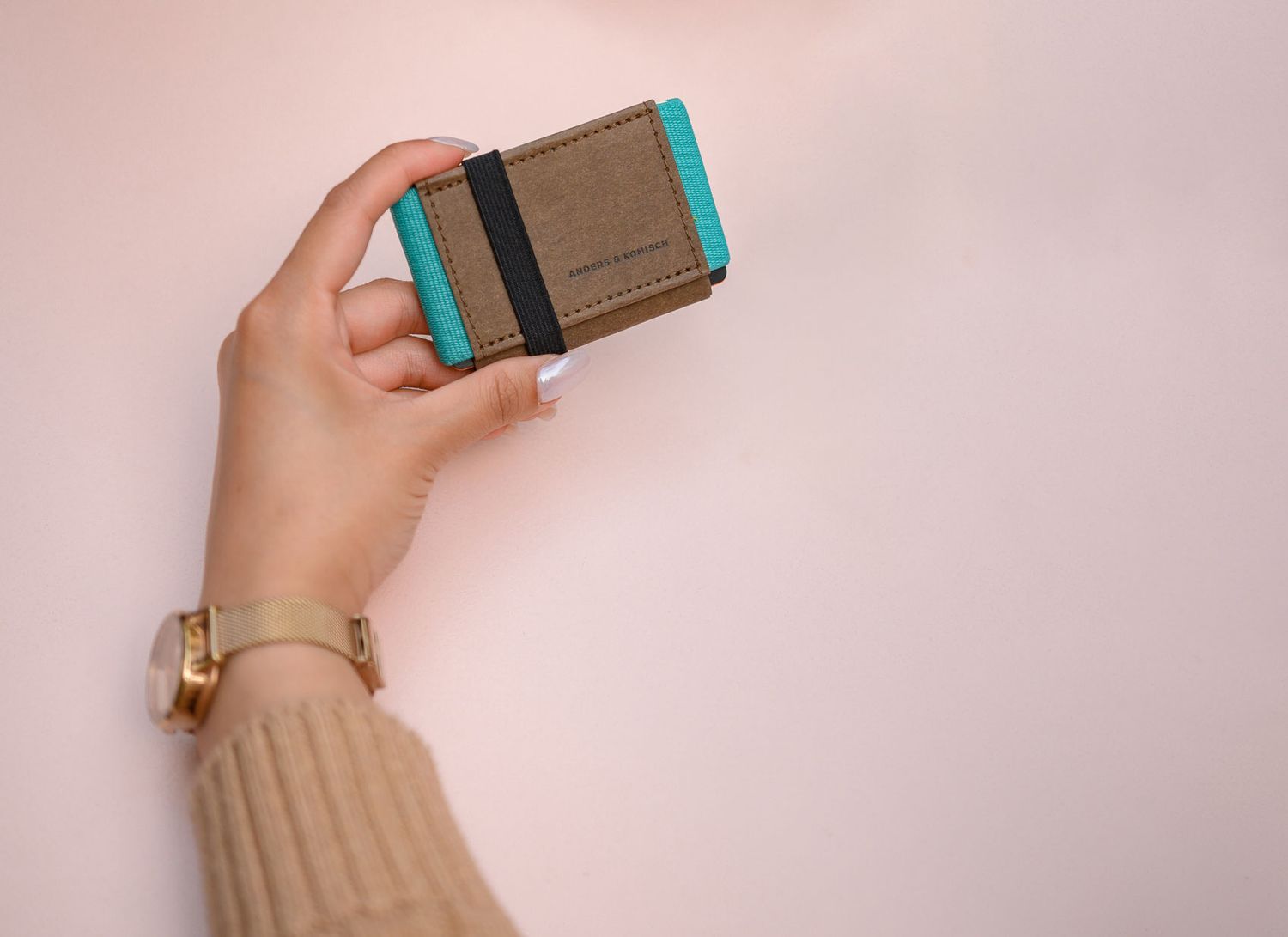 Hand holding slim brown leather wallet against pink background.