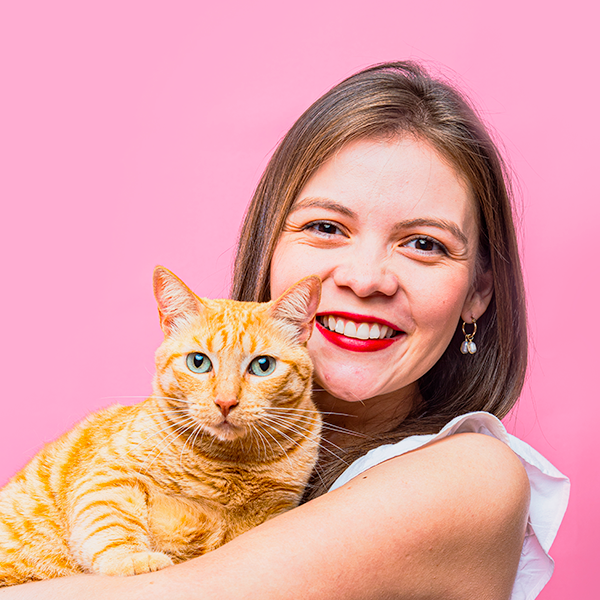 Orange tabby cat being held against pink background while showing affection.