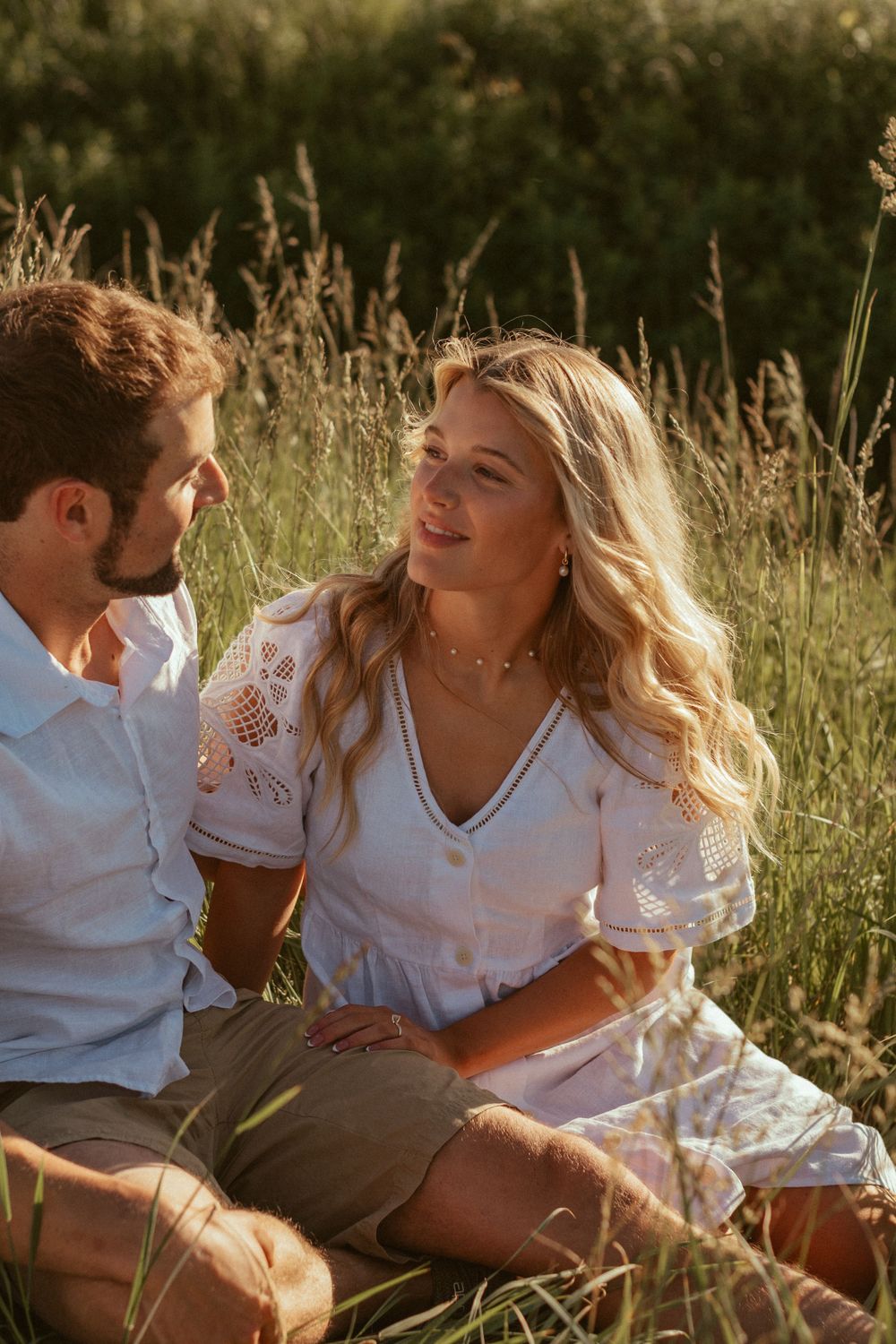 Couple sitting in tall grass field sharing intimate moment in summer sunlight.