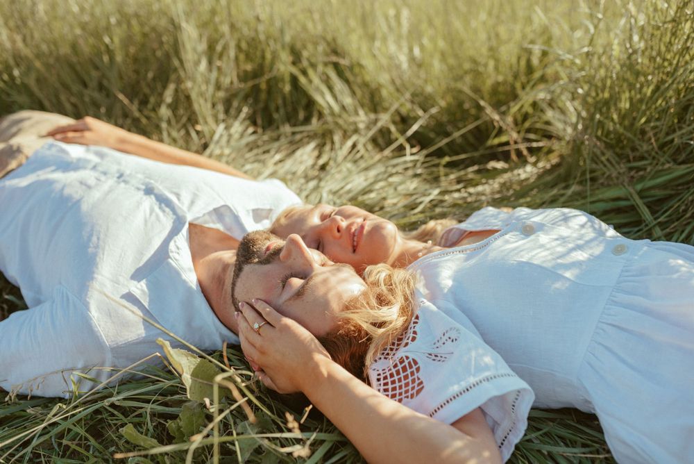 Person in white dress lying in summer grass field with hands behind head.