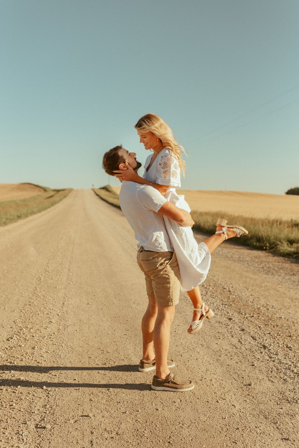 A romantic moment captured on a dirt road as a couple embraces in the warm sunlight.