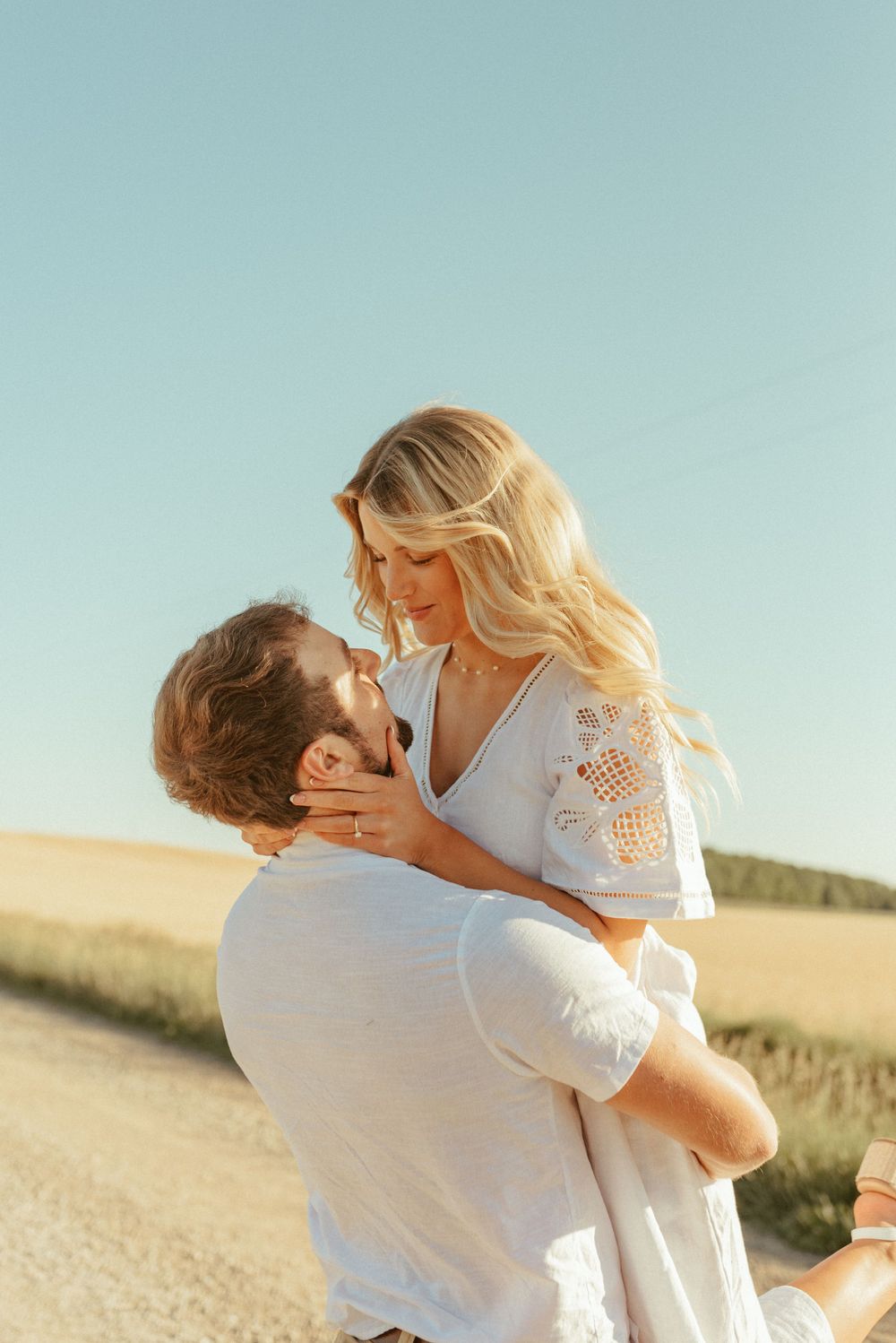 An intimate portrait of a couple sharing a tender moment on a rural path at sunset.