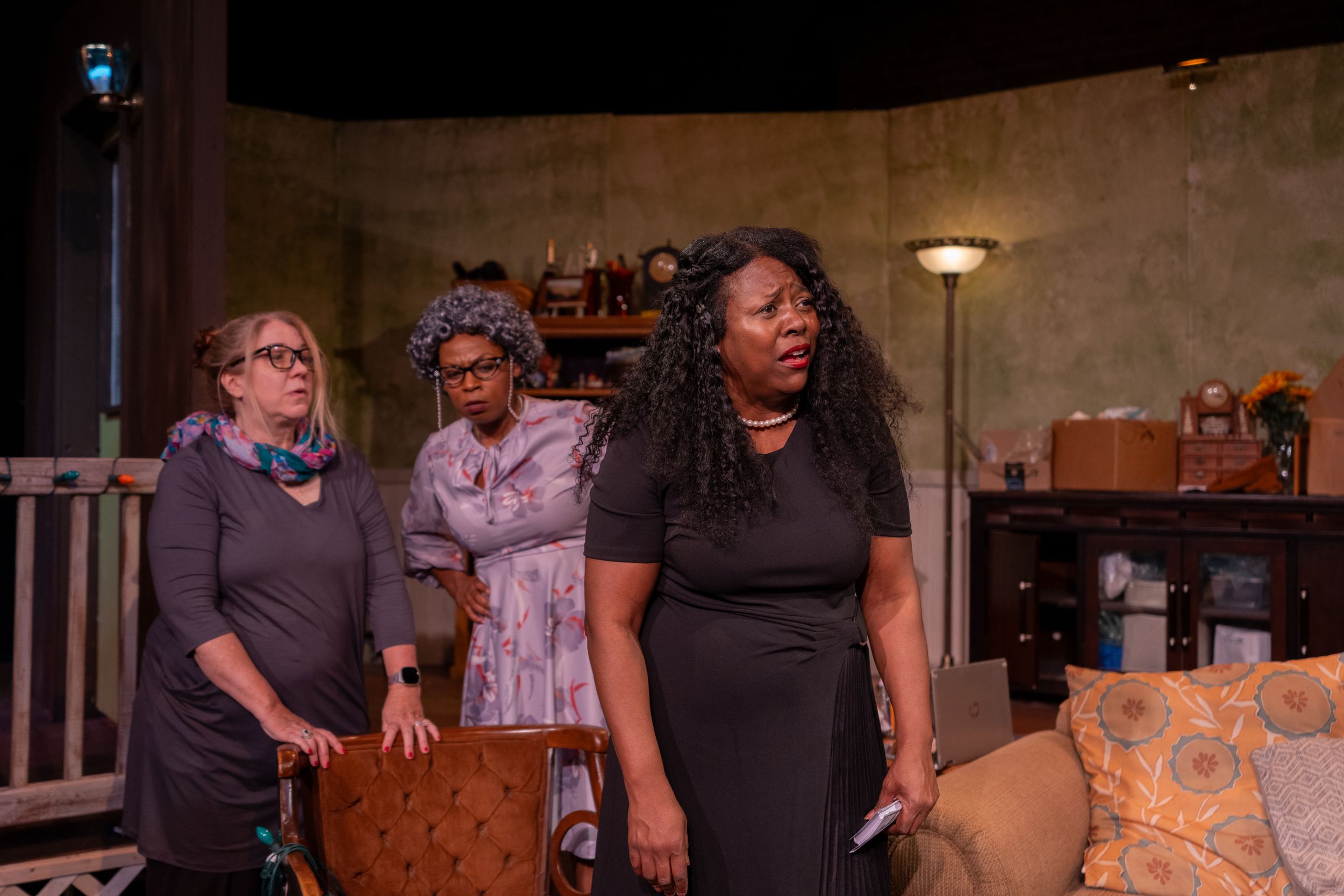 Three performers act out a dramatic scene in a staged living room setting.