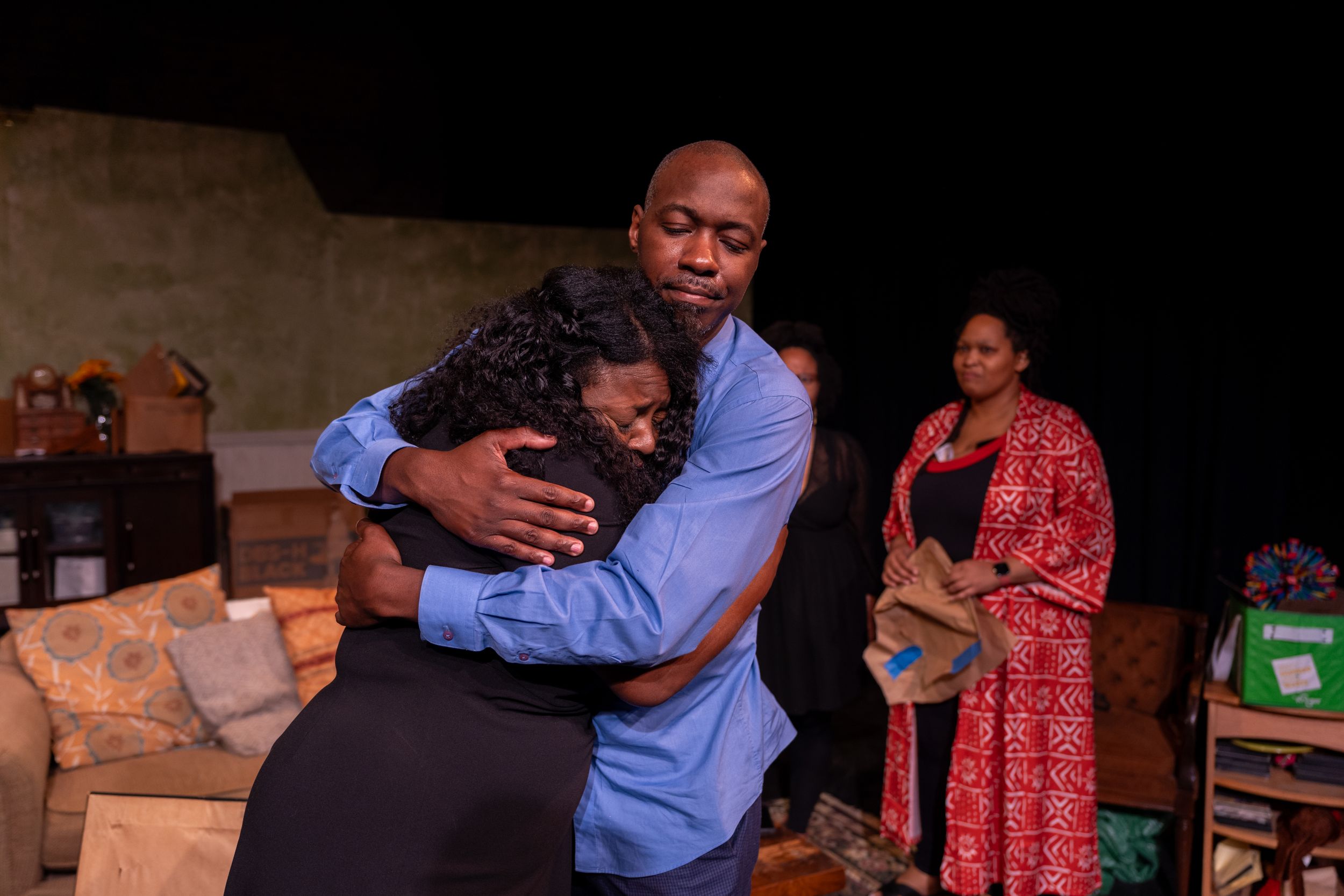 An emotional embrace scene plays out on stage with dramatic lighting.