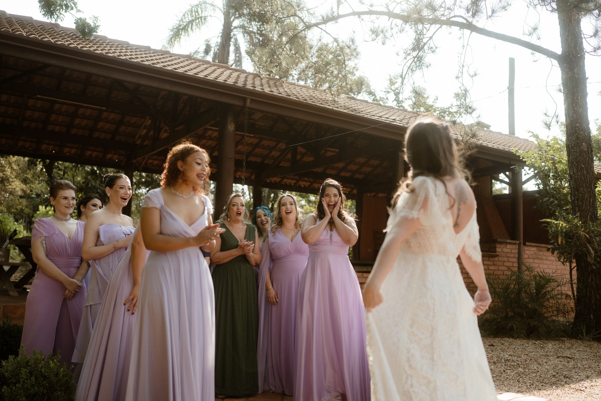 Wedding party in purple bridesmaid dresses gather outdoors under covered patio.