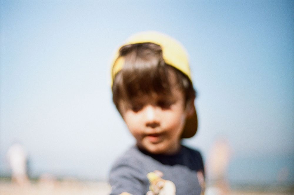 Young child wearing a yellow cap at the beach on a sunny day, blurred foreground focus effect.