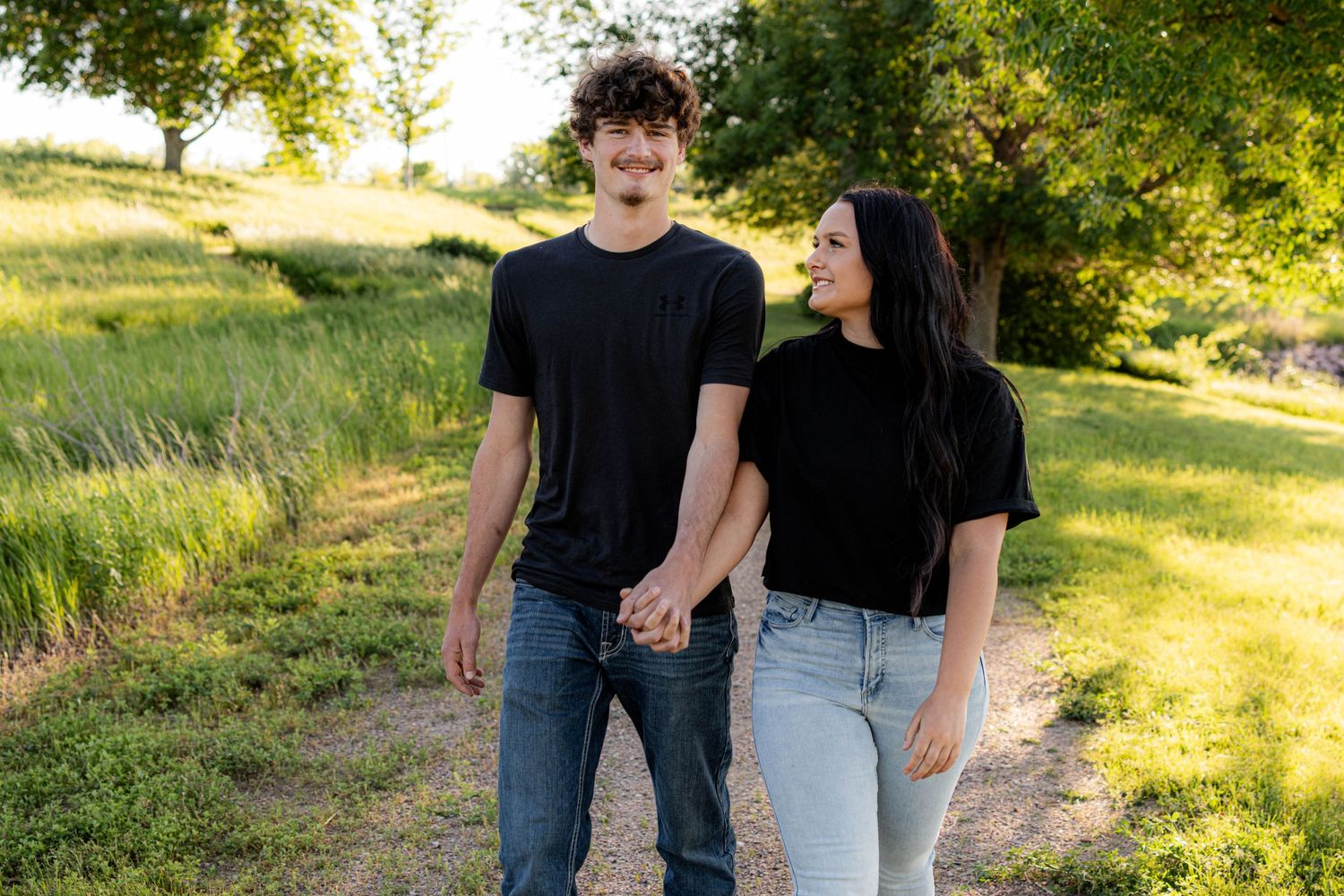 Casual couples photo shoot in a sunny outdoor setting with natural greenery.