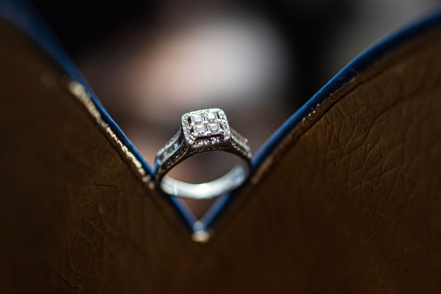 Diamond halo engagement ring displayed in a brown leather ring box with blue velvet lining.
