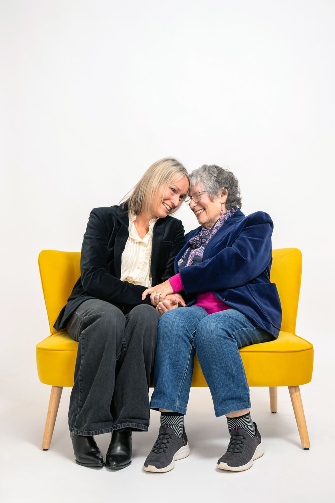 Two people sharing intimate moment while sitting on yellow chairs against white background.