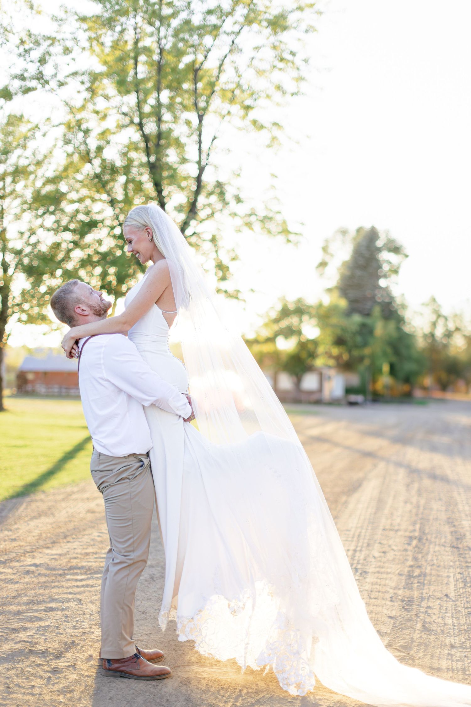 Romantic sunset wedding photo with flowing veil on country road.
