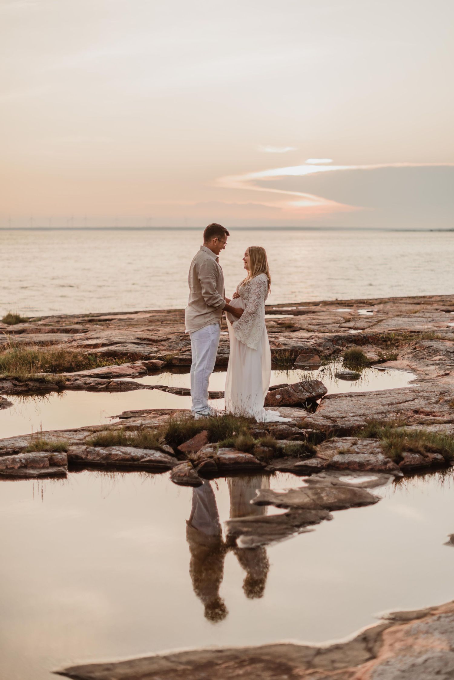 Romantic sunset maternity photo on rocky cliff overlooking water.