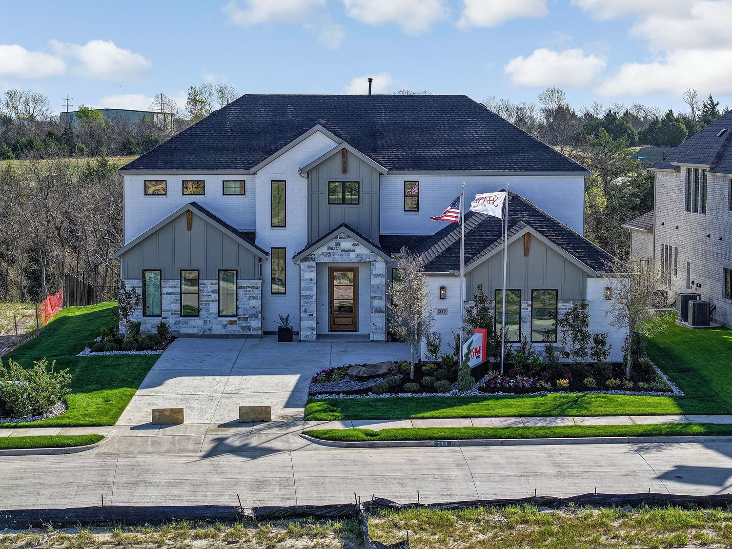 Modern ranch home with warm glowing windows at dusk, surrounded by tall pine trees and featuring gray siding.