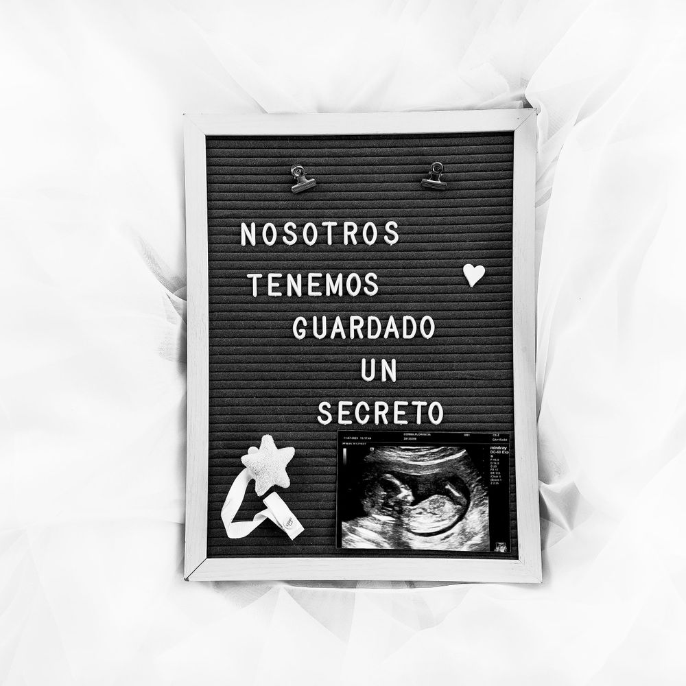 Black letterboard with Spanish text and ultrasound photo announcing pregnancy news.