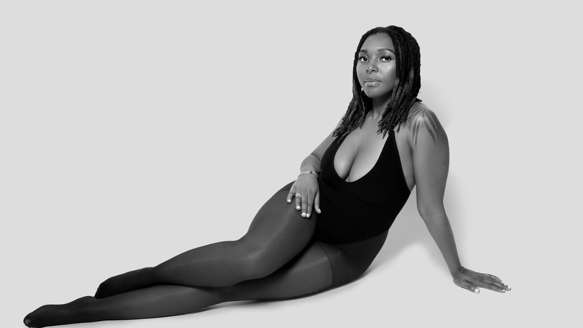 High contrast black and white portrait of a person in a black leotard posing gracefully on the floor.