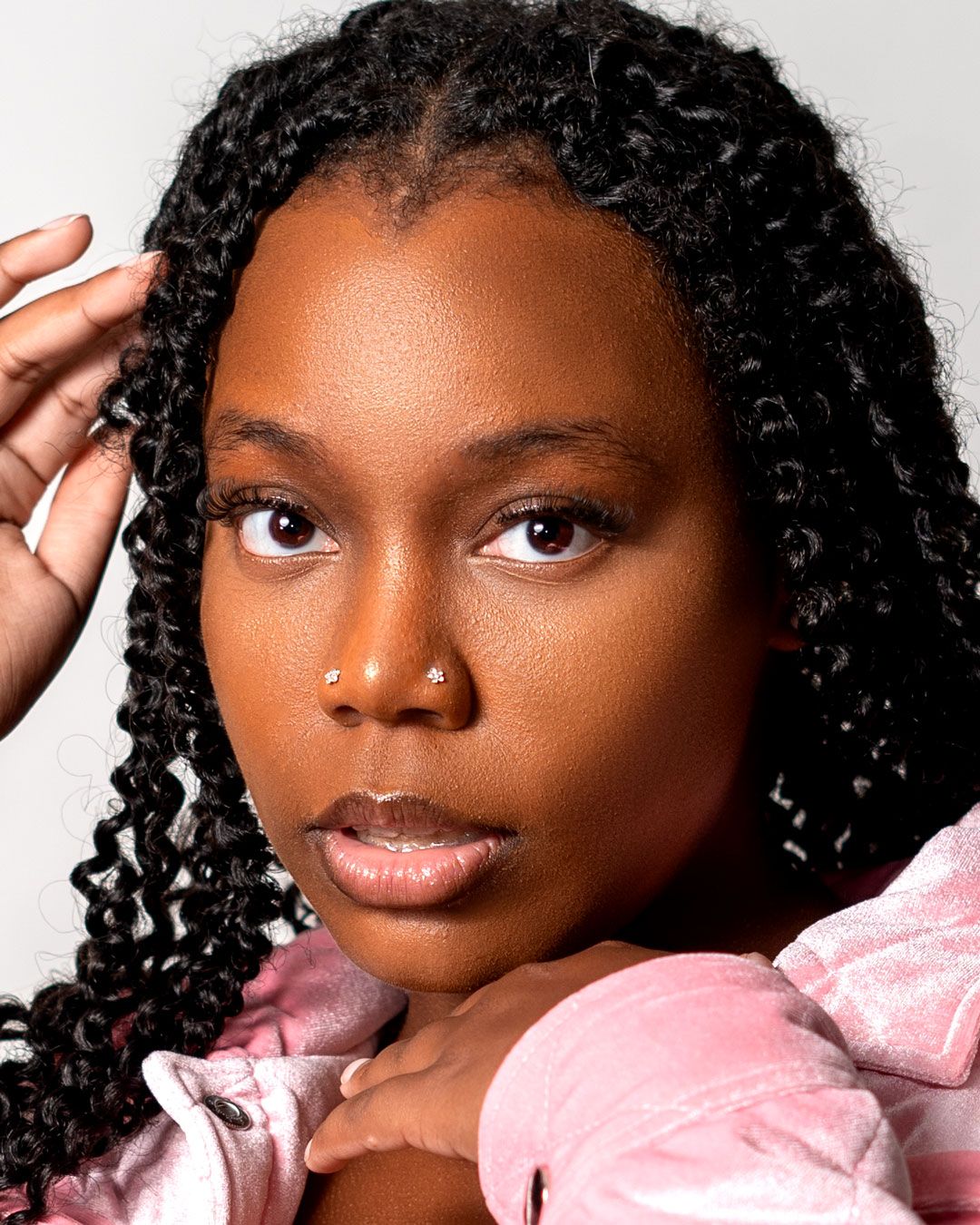 Portrait of someone with glowing skin wearing pink velvet and styled with beautiful long twisted curls.