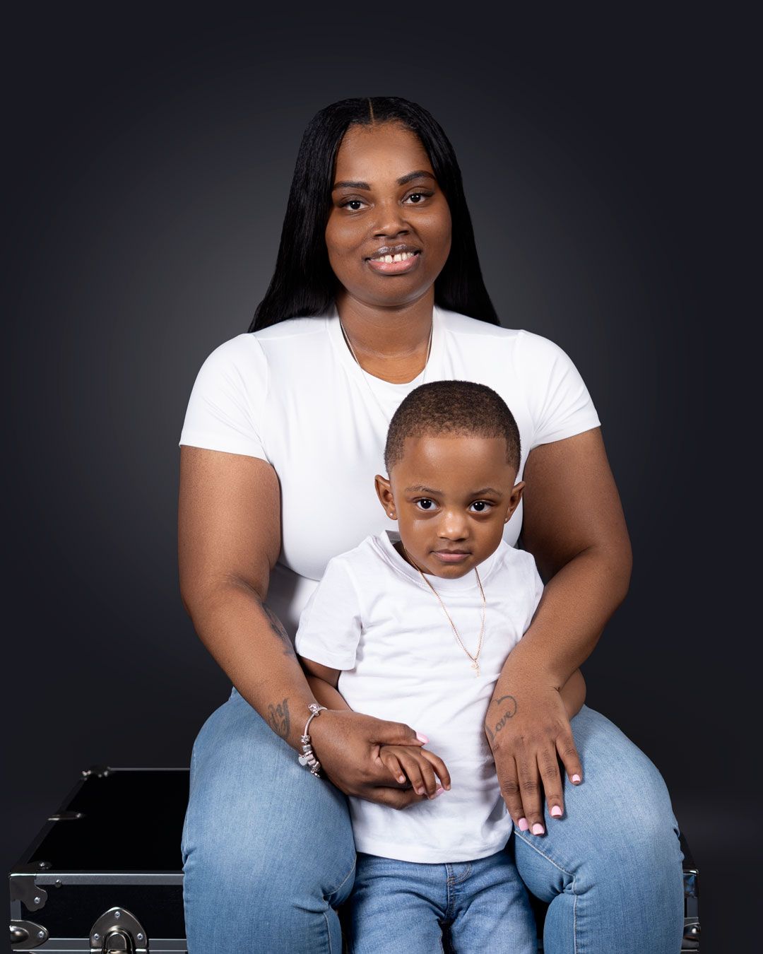 A woman and young boy in matching white shirts and jeans pose together for a professional studio portrait.