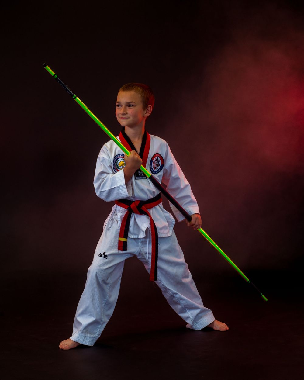 Martial artist performs with glowing green weapon against dark background.
