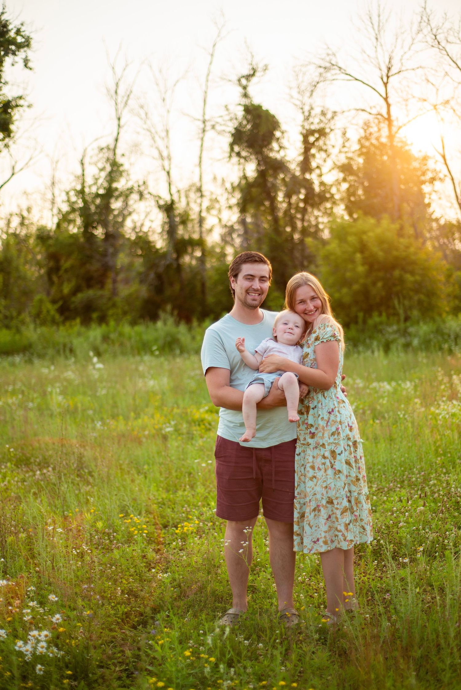A family stands together in a sunlit meadow during a summer evening photo session.