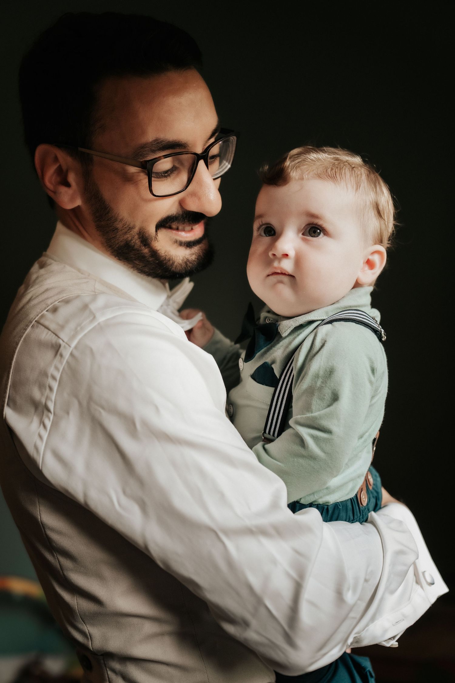 Portrait of parent in glasses holding young child wearing formal outfit.