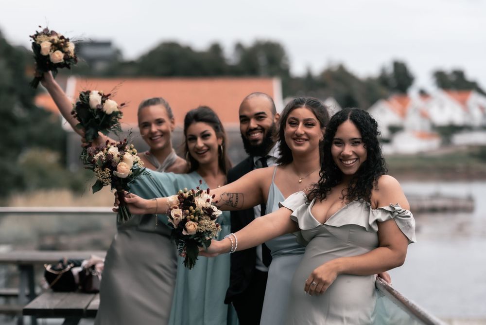 A group in light blue and gray formal attire poses on a waterfront while holding floral bouquets.
