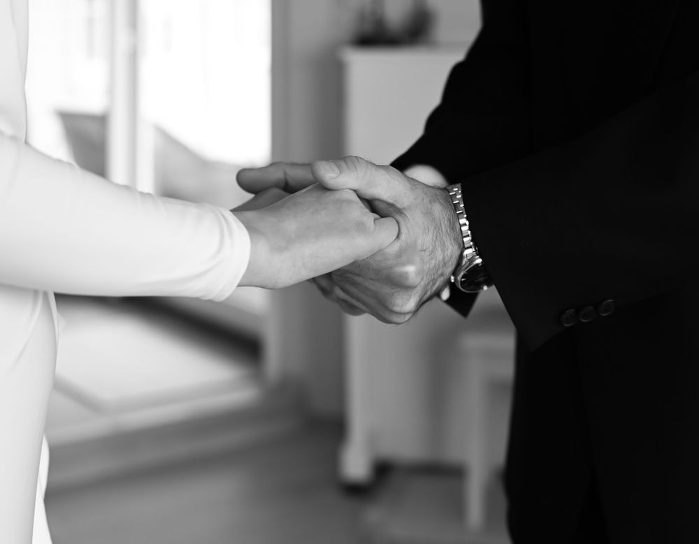 Black and white close-up image of two hands clasping together, one wearing a bracelet.