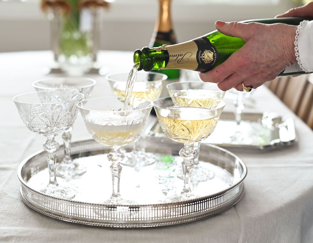 Champagne being poured into vintage crystal coupe glasses arranged on an elegant silver serving tray.