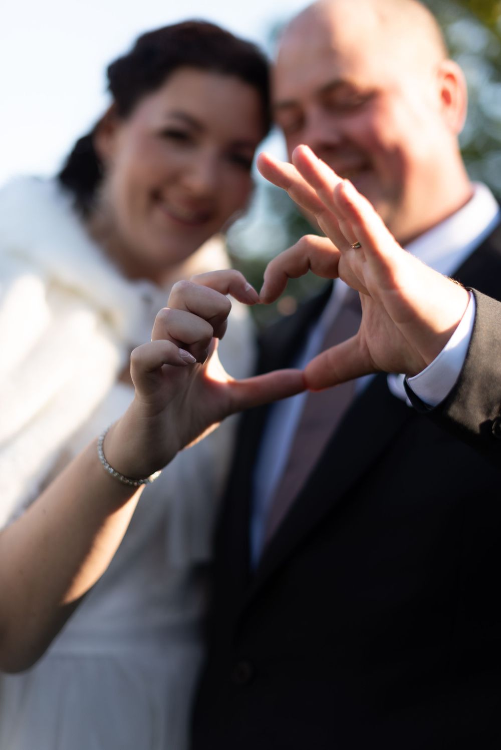 Wedding couple making a heart shape with their hands in soft focus.