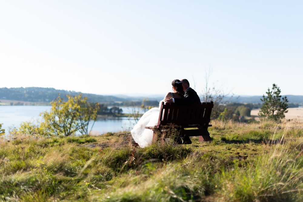 Silhouette of newlyweds sitting on bench overlooking lake during sunset.