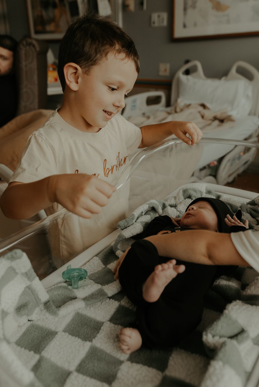 Child looking down at newborn sibling in hospital bed.