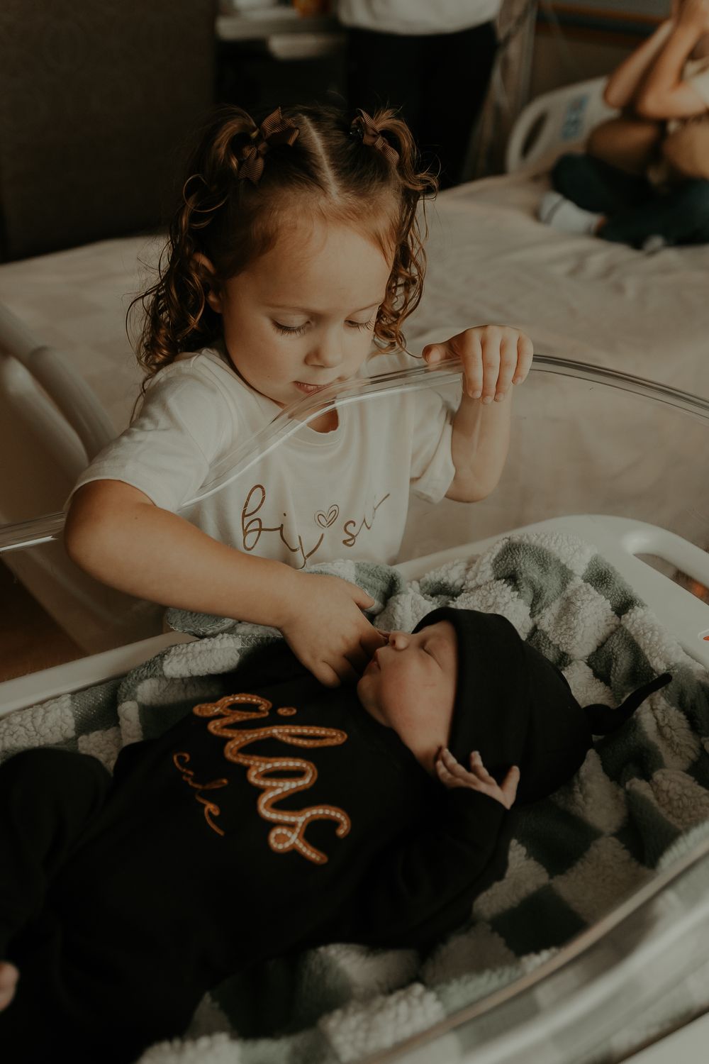 Young child gently touching newborn sibling in hospital setting.