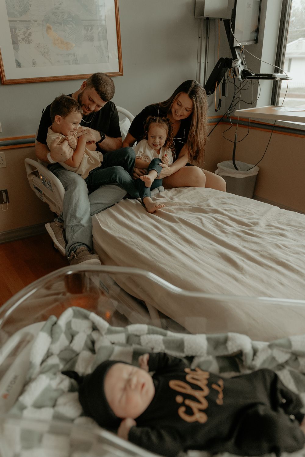 Family gathered around hospital bed with newborn in muted lighting.