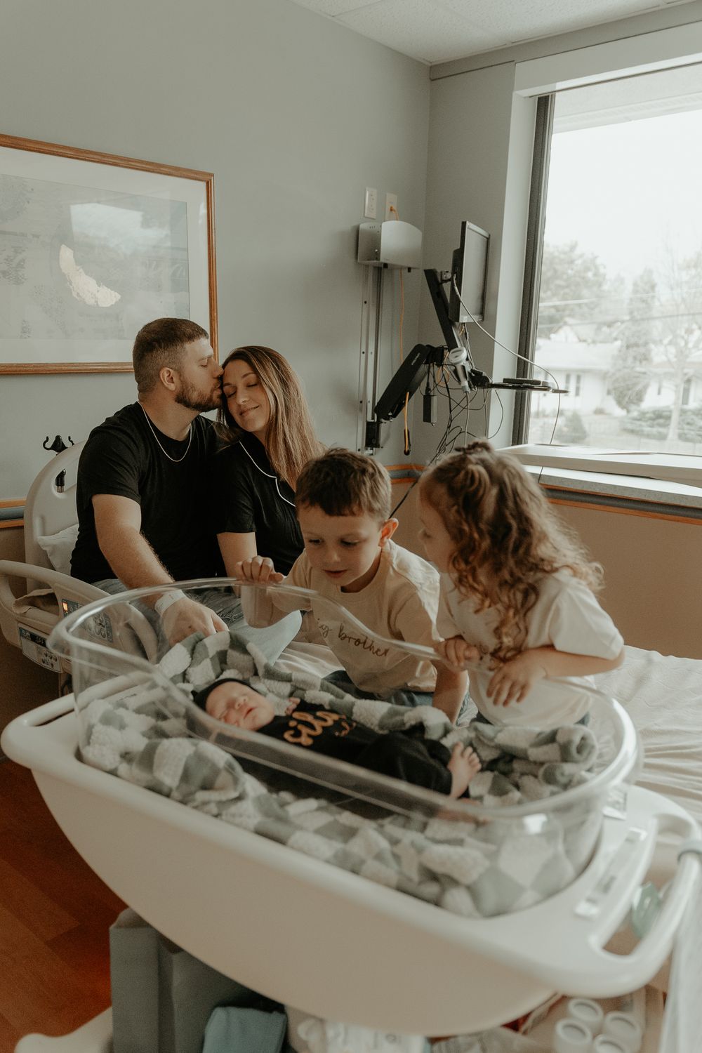 Family members gathered around hospital bassinet sharing intimate moment.