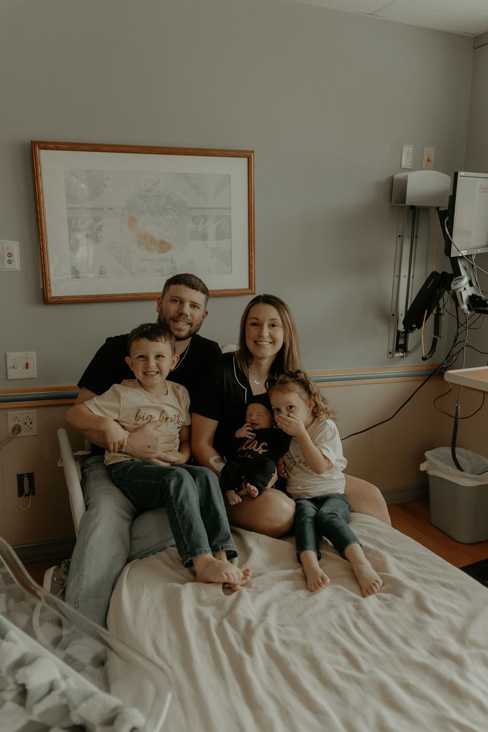 Family members cuddle together on a white hospital bed during a special moment.