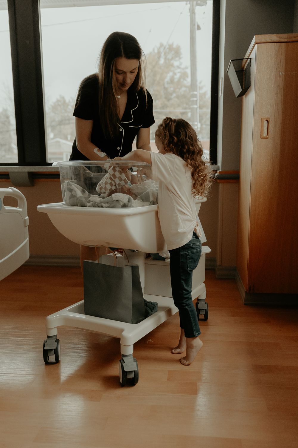 A hospital bassinet being moved across a wooden floor during a newborn care session.