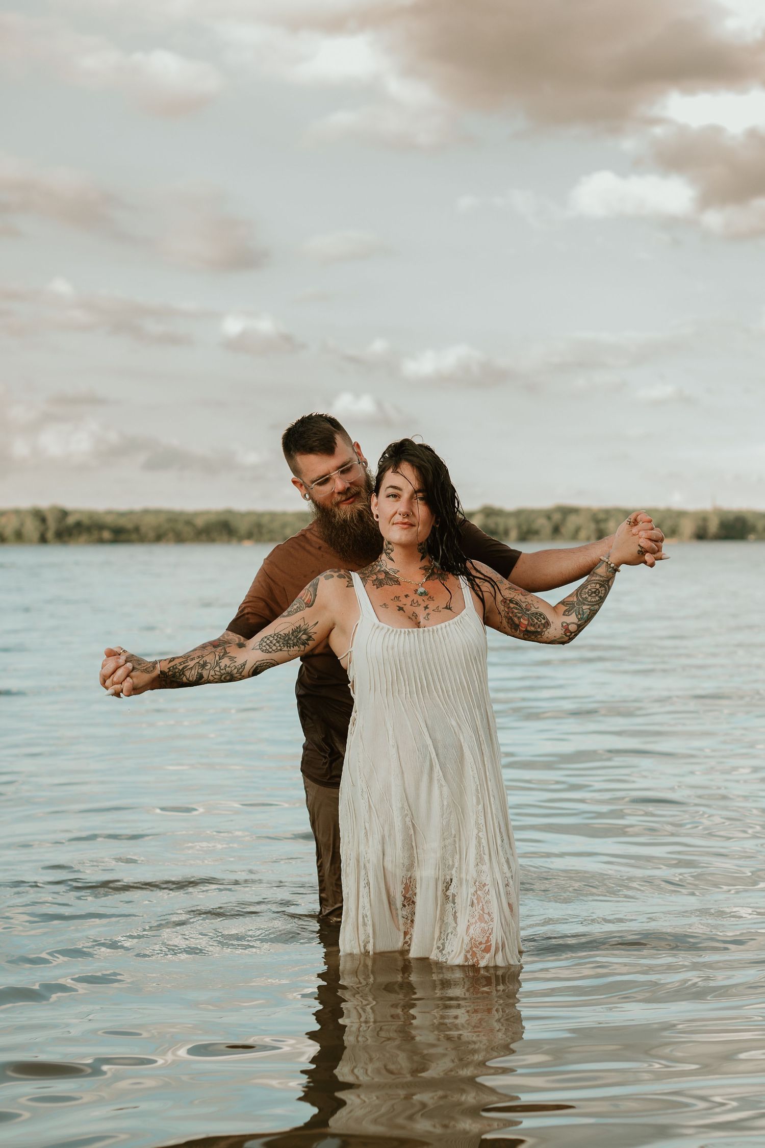 A couple enjoys a romantic moment while wading in a serene lake at sunset.