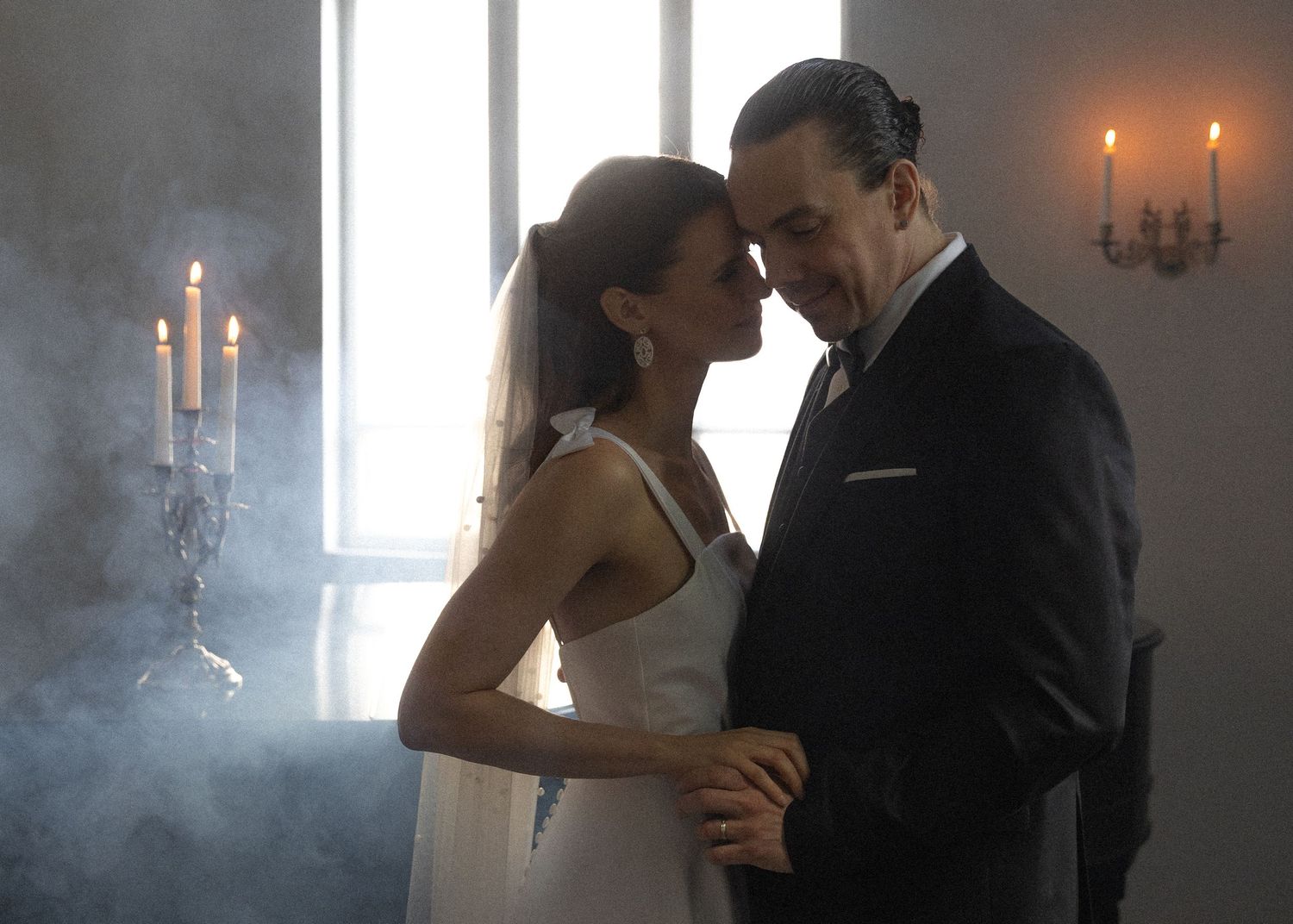 A romantic couple in formal attire share an intimate moment while dancing in a dreamy candlelit room with fog effects.
