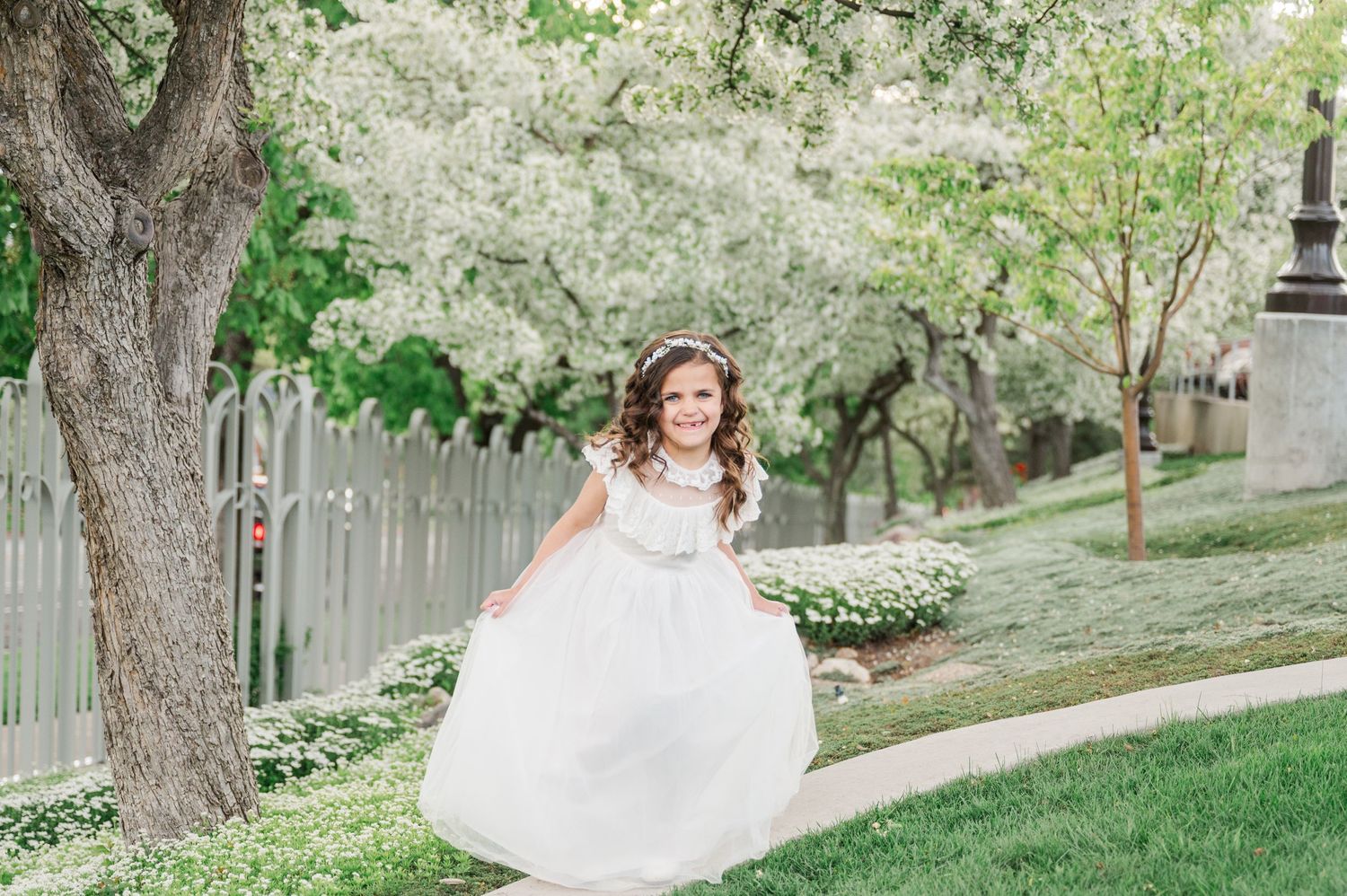 Joyful twirl in white dress against backdrop of spring trees and garden path.