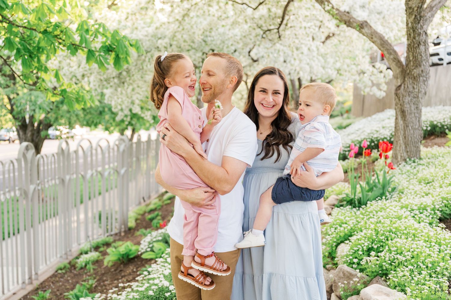 Family portrait in blooming spring garden with white picket fence and tulips.
