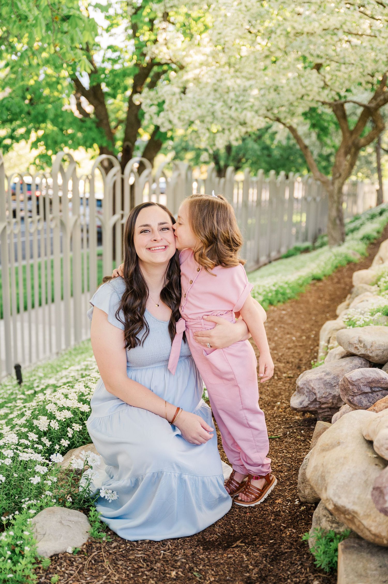 Sweet moment between parent and child in spring garden setting with white fence.
