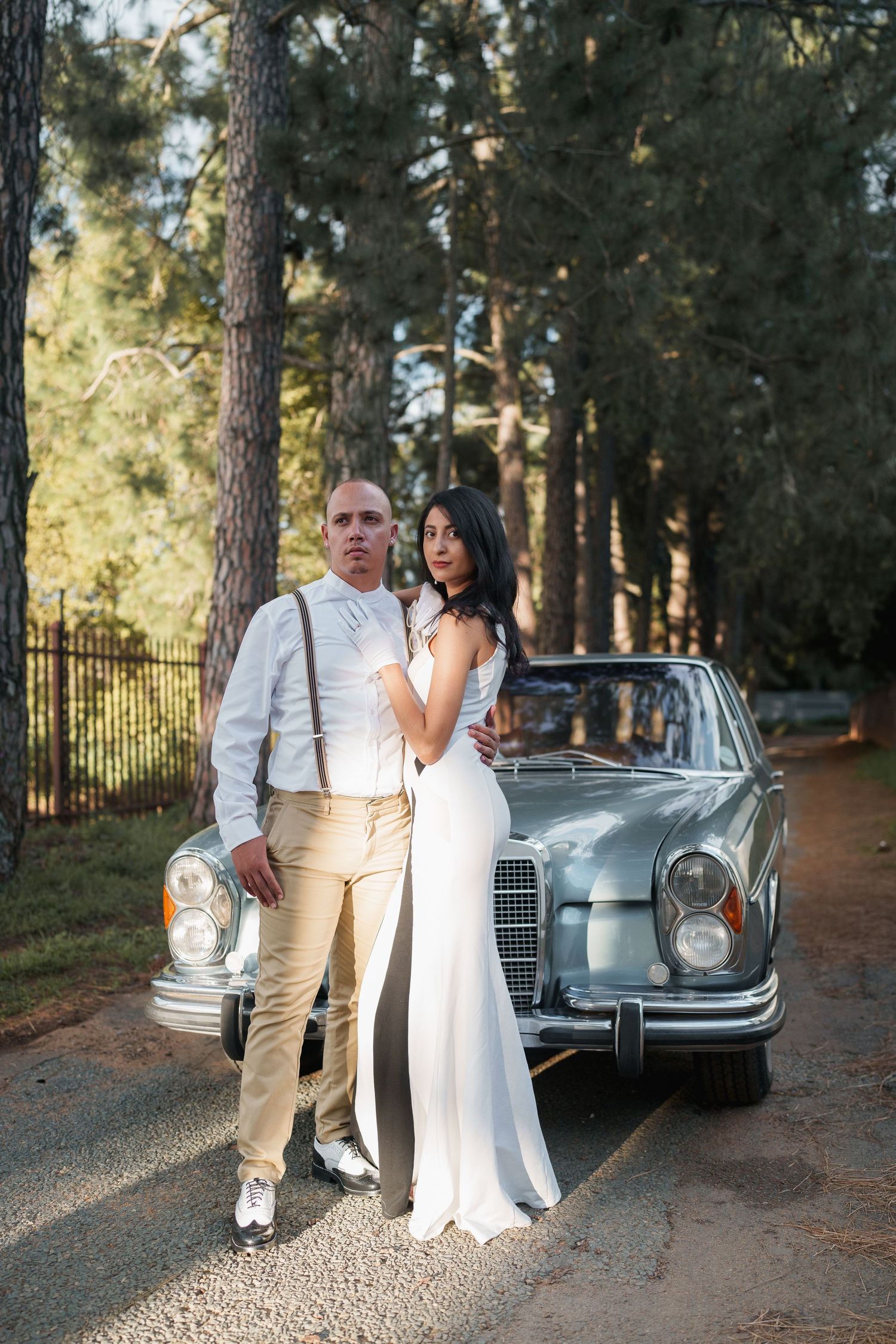 Elegant couple poses with vintage Mercedes-Benz car in a wooded setting.