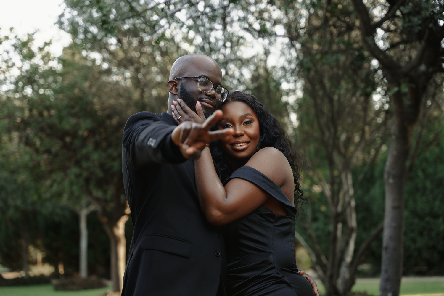 A couple in black formal attire shares a playful moment in an outdoor setting.