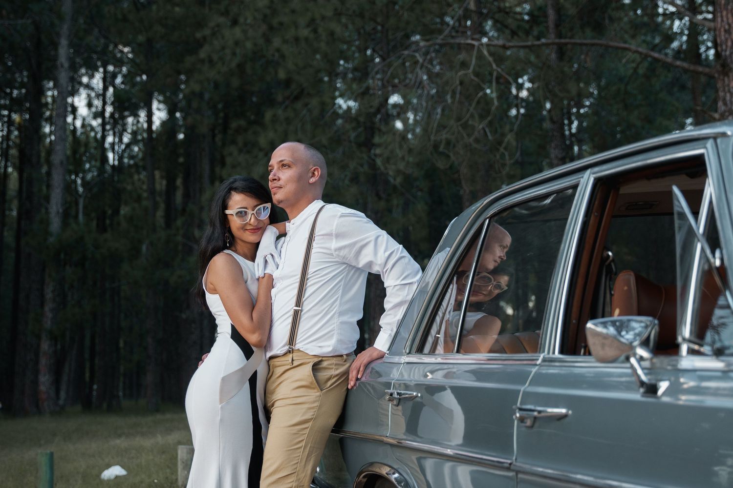 Happy couple sharing a moment near classic car in forest setting.