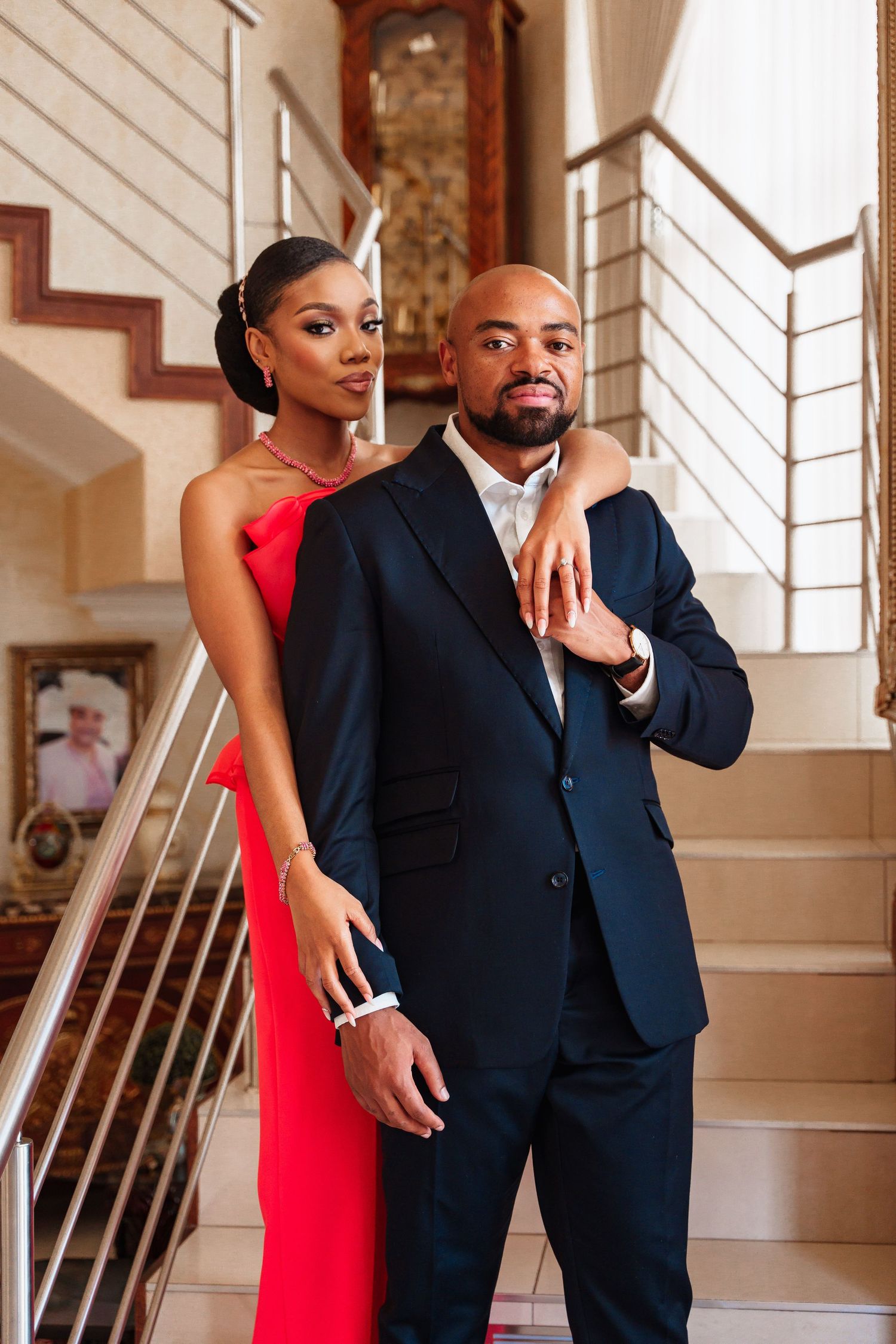 Elegant couple posing on staircase, woman in red dress and man in navy suit.