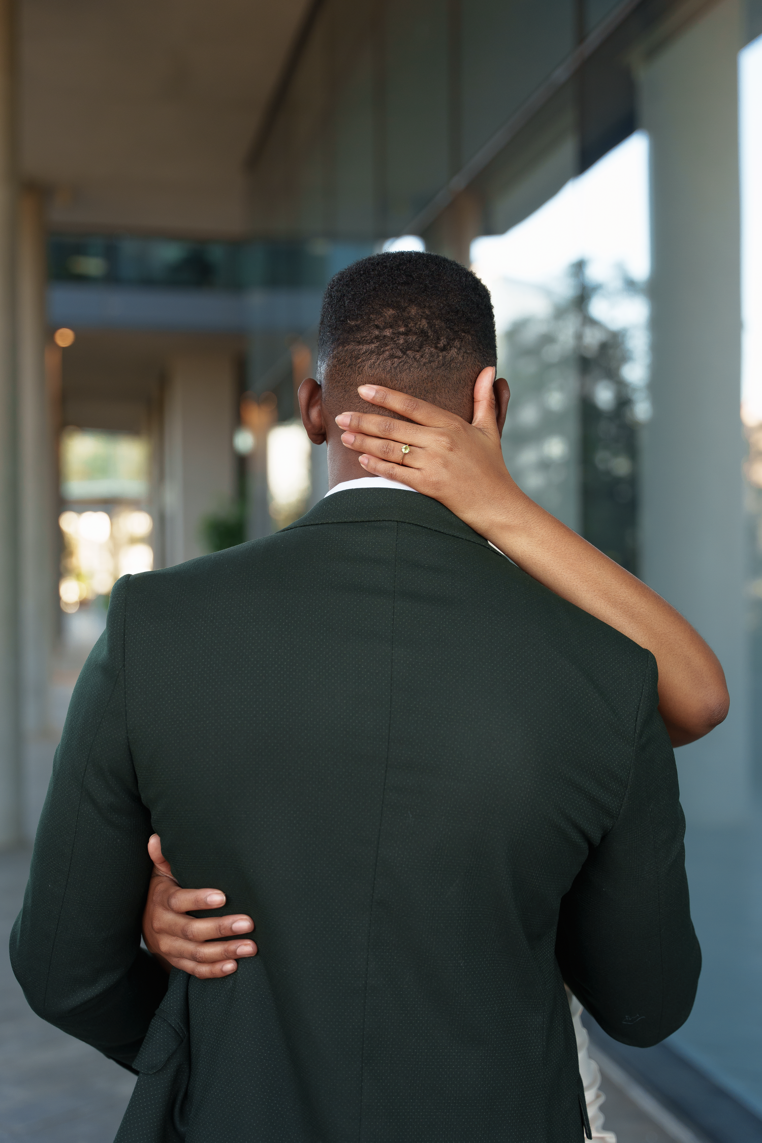 Back view of couple embracing in formal wear against modern building.