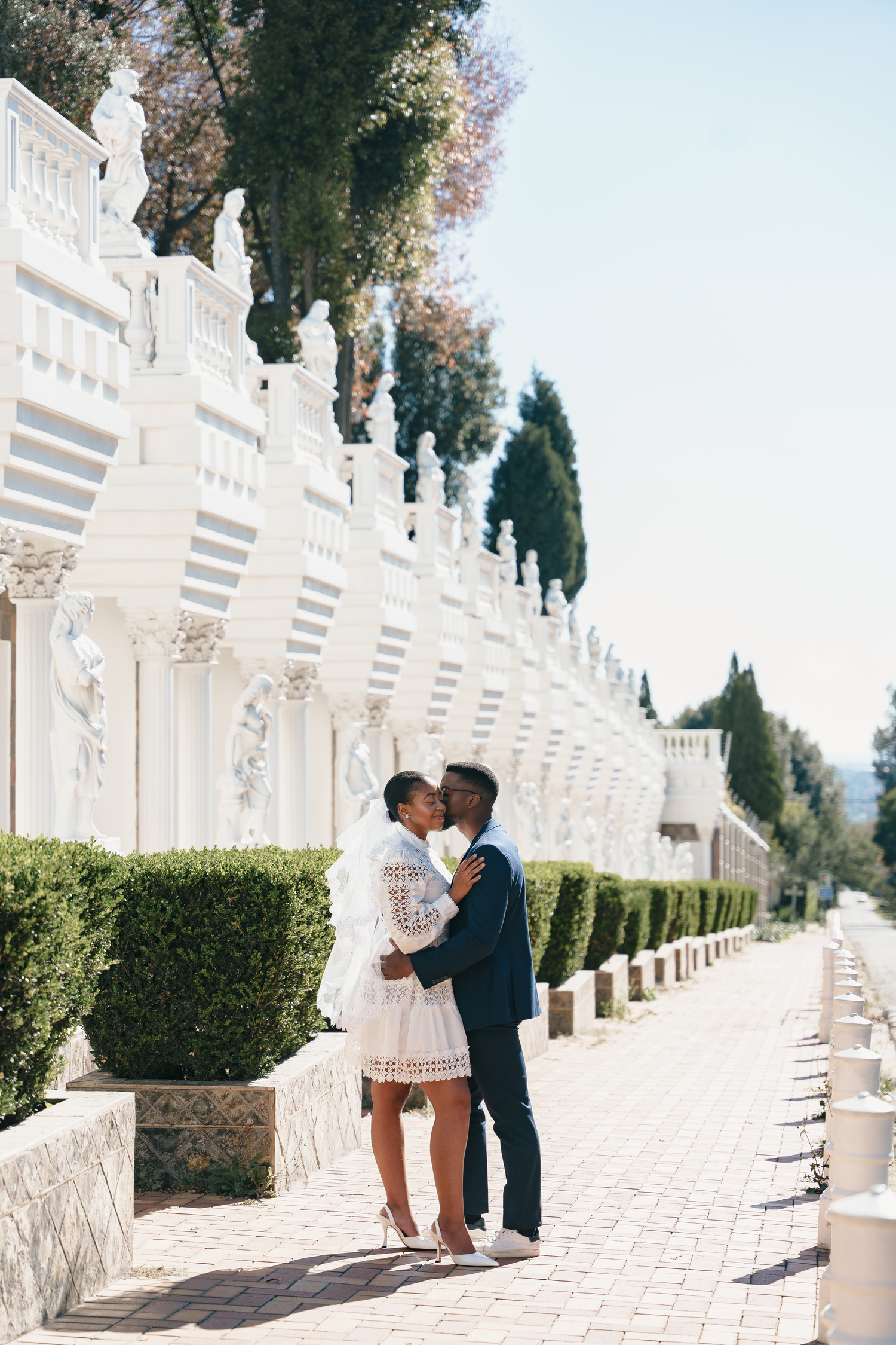 Romantic couple sharing kiss in elegant white colonnade garden setting.